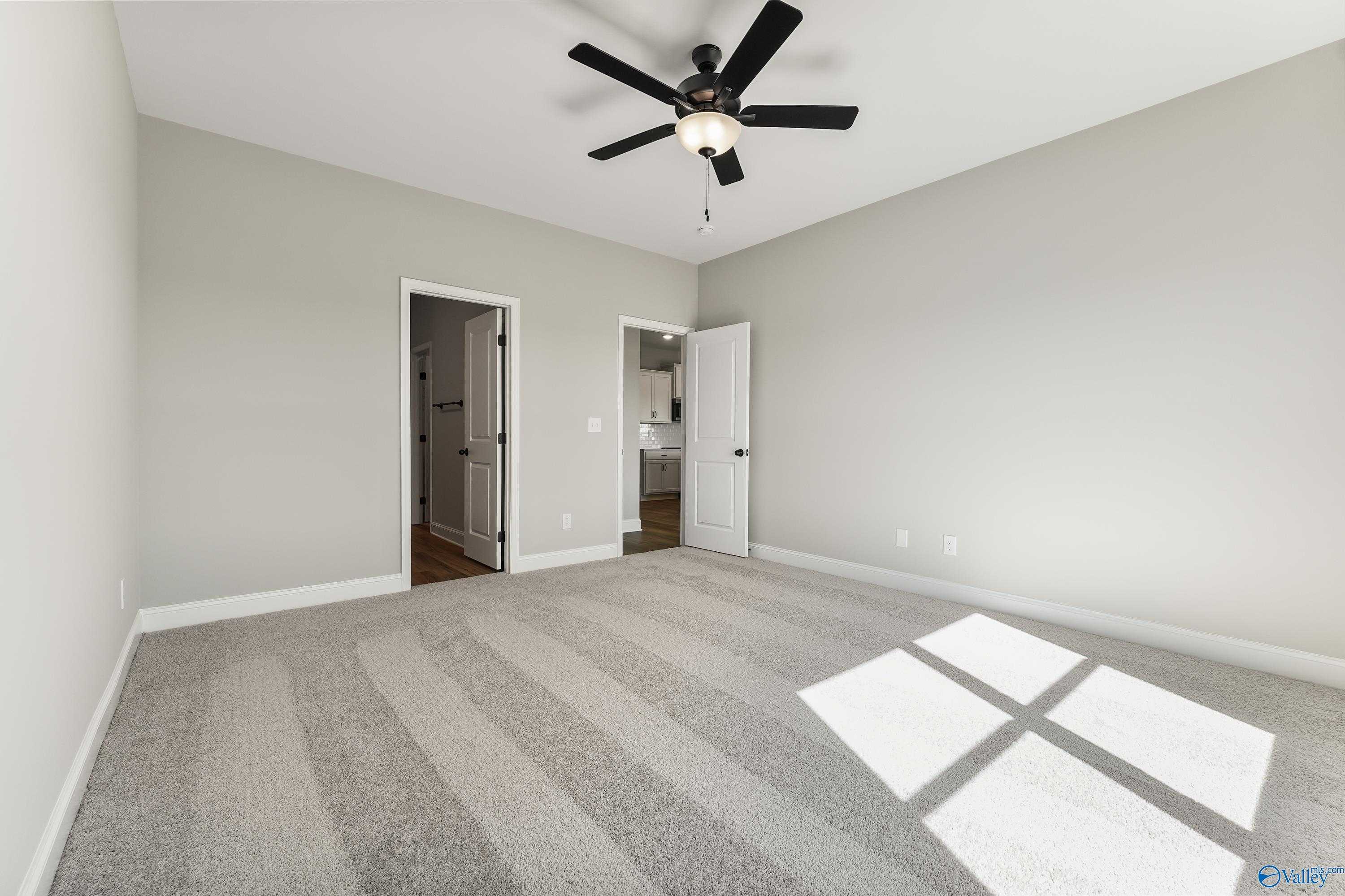 Bright bedroom with ceiling fan, light gray walls, beige carpet, and en-suite bath doors in Davidson Homes The Daphne C, Hazel Green, AL