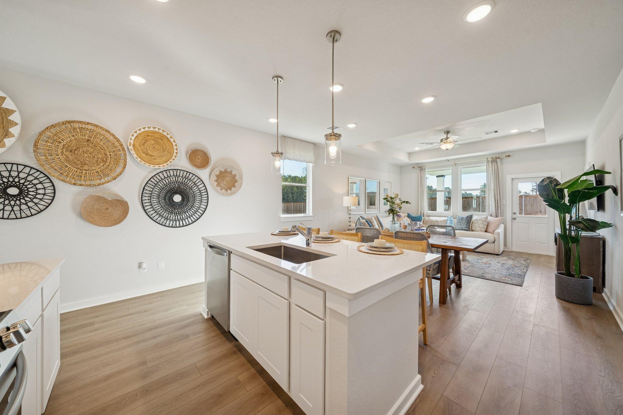 Open-concept kitchen living room at Spring Branch Crossing in Conroe Texas with white island hardwood floors woven baskets and plants