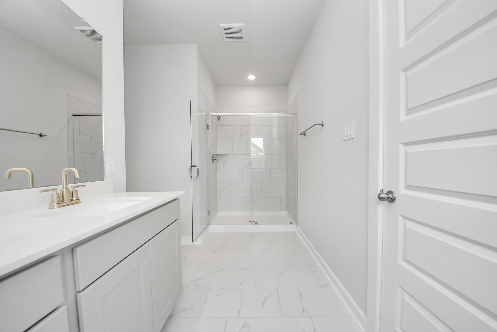 Modern bathroom with glass-enclosed walk-in shower and marble-style tile in The Verano B home at Sunterra, Katy, Texas.