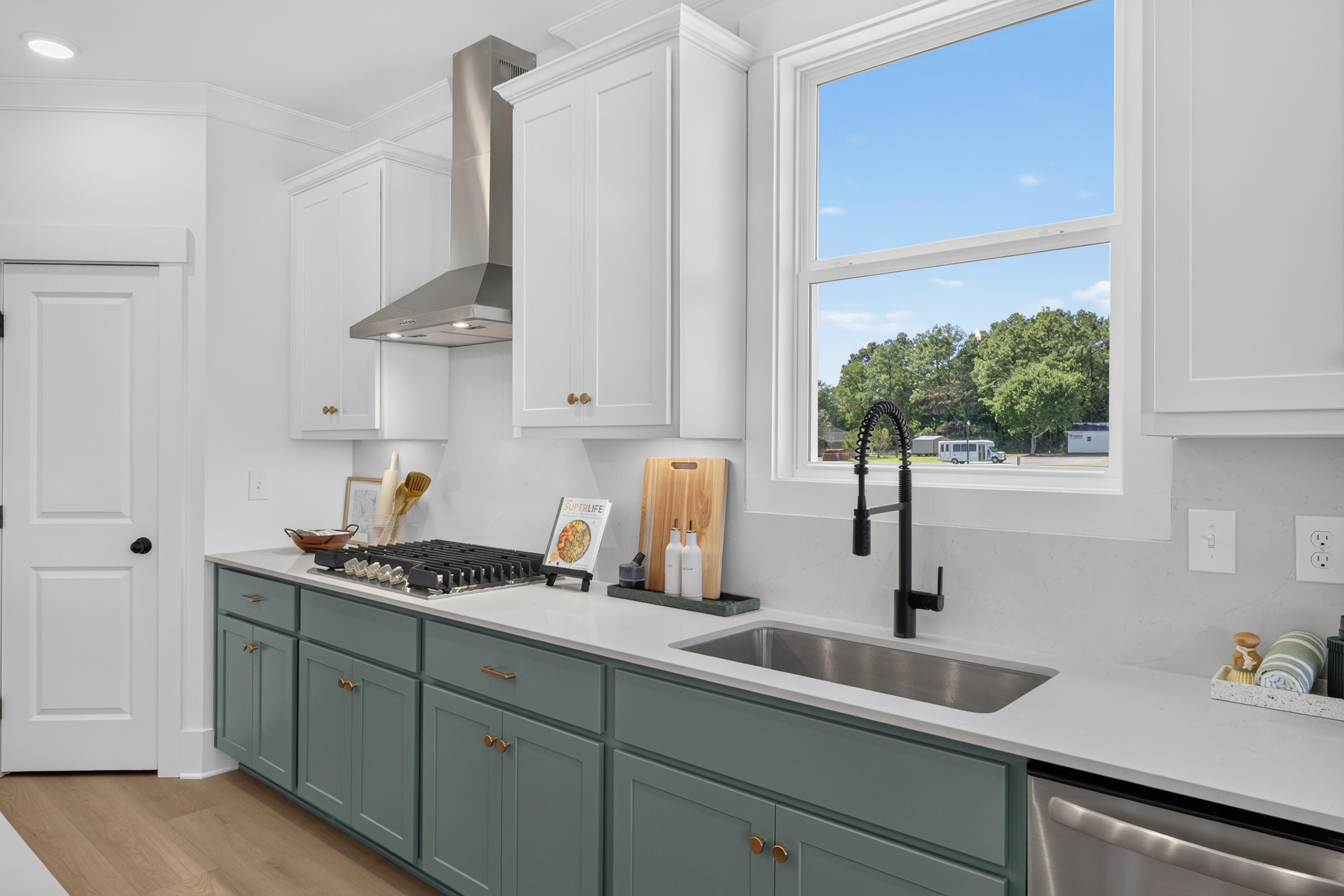 Kitchen with sage green cabinets, white countertops, gas cooktop, and black faucet at Evergreen Mill in Madison, Alabama by Davidson Homes