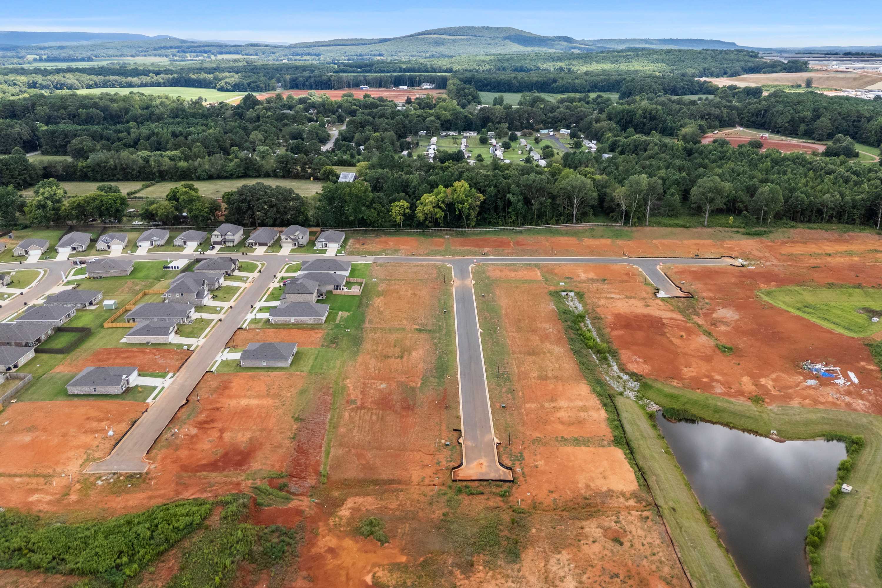Aerial view of Wood Trail neighborhood in Toney Alabama with new homes, red dirt roads, pond, and green fields by Davidson Homes