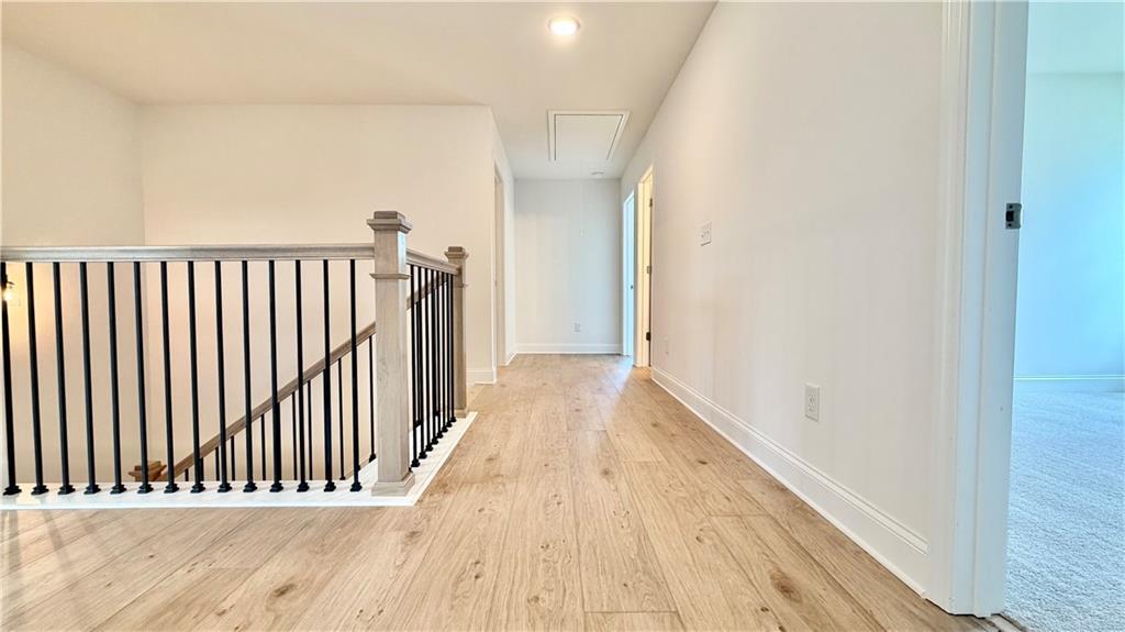Bright second-floor hallway with wood-look flooring and modern railing in The Hickory C floor plan, Wehunt Meadows.