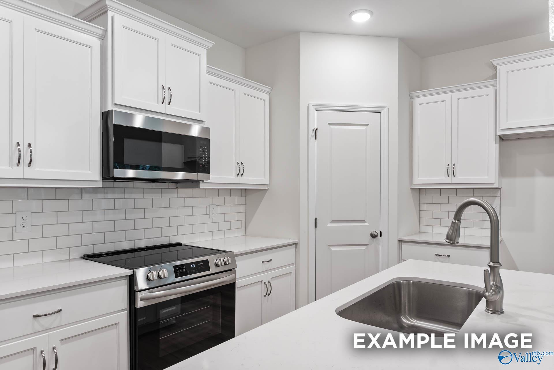 Modern kitchen with white cabinets, stainless appliances, and subway tile backsplash in The Daphne C, Spragins Cove home.