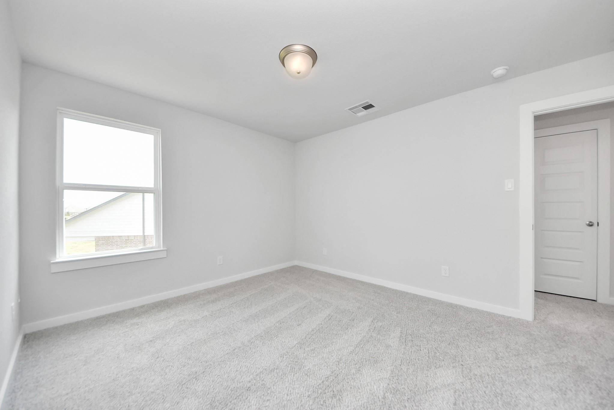 Spacious, bright secondary bedroom with neutral carpet and walls in The Verano B floor plan at Sunterra, Katy, Texas.
