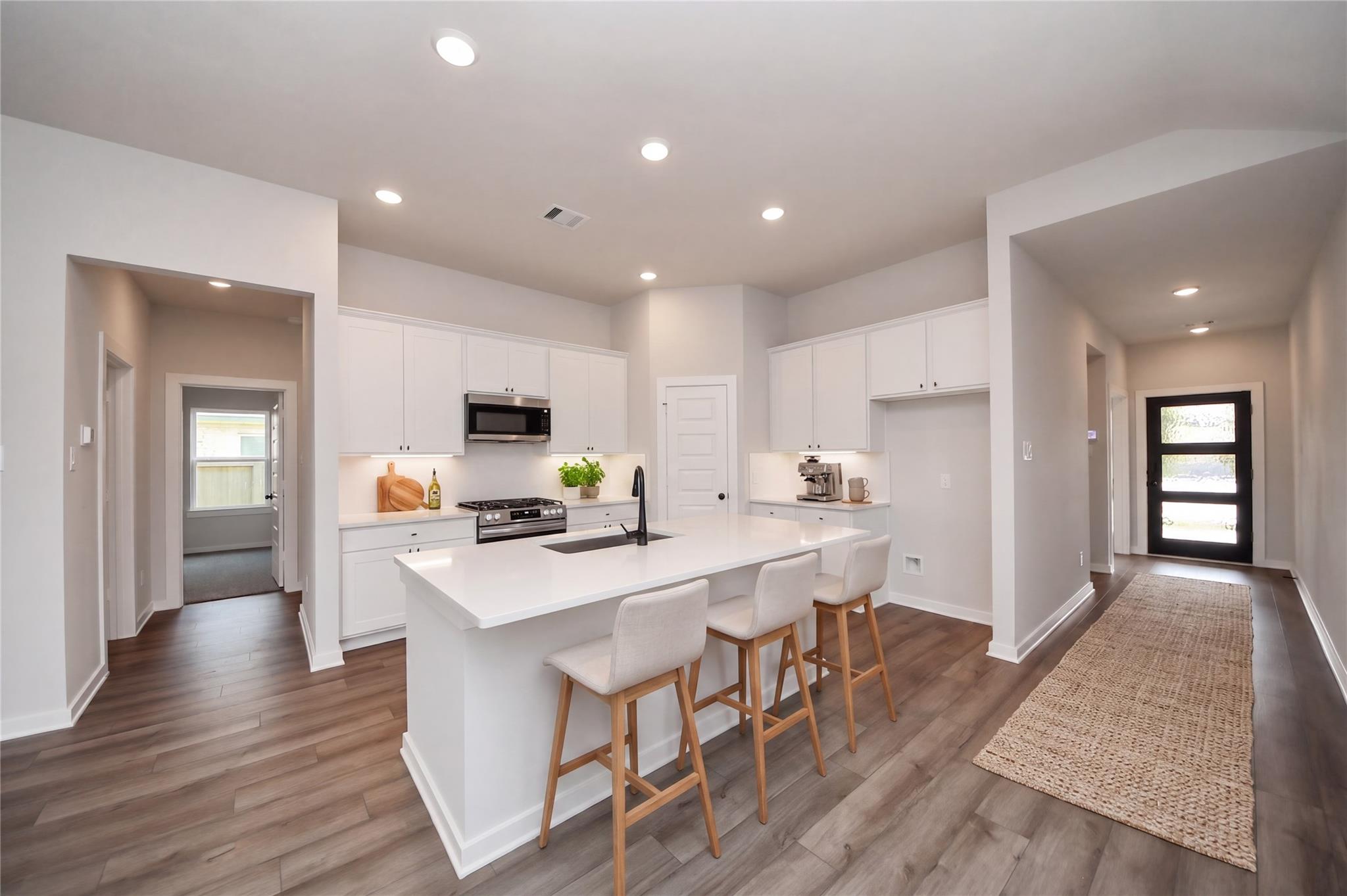 Modern white kitchen with island, bar seating, and stainless steel appliances in The Riviera C home, River Ranch Meadows.