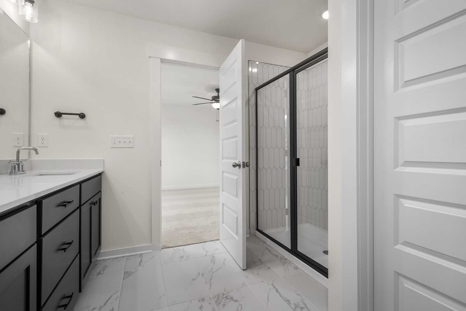 Modern master bathroom featuring double vanity, glass shower enclosure, and bedroom access in Davidson Homes The Logan C, Gallatin, TN