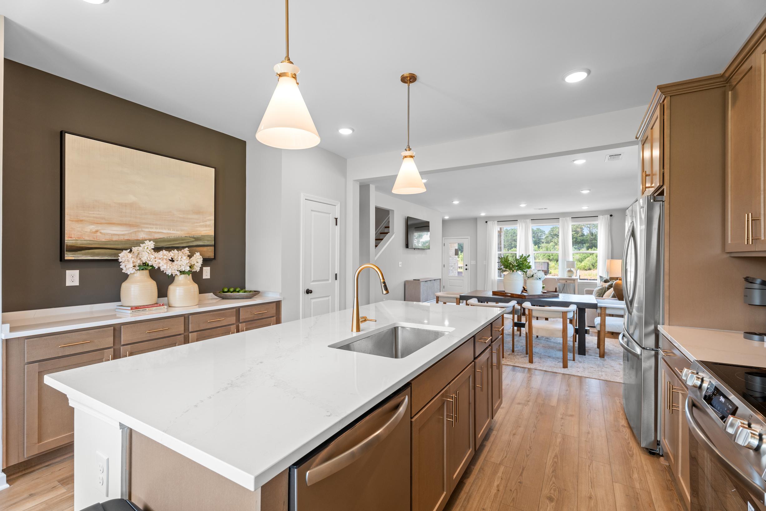Modern kitchen with white quartz island, wood cabinets, and open-concept dining area at Links Crossing in Auburn, Alabama.