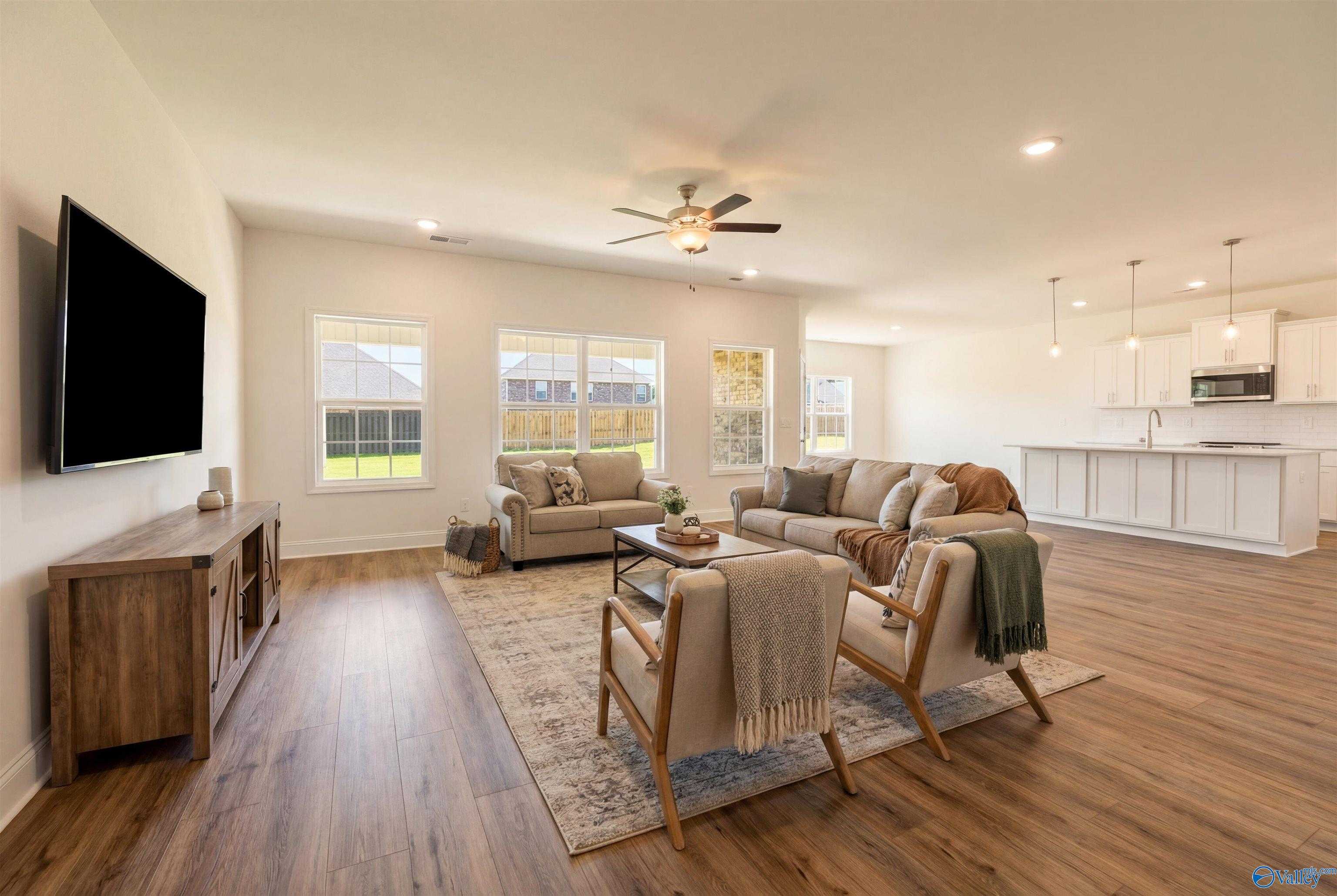 Open-concept living room with beige sectional sofa, wooden coffee table, and large windows overlooking backyard in Davidson Homes The Rockford B, Toney, Alabama