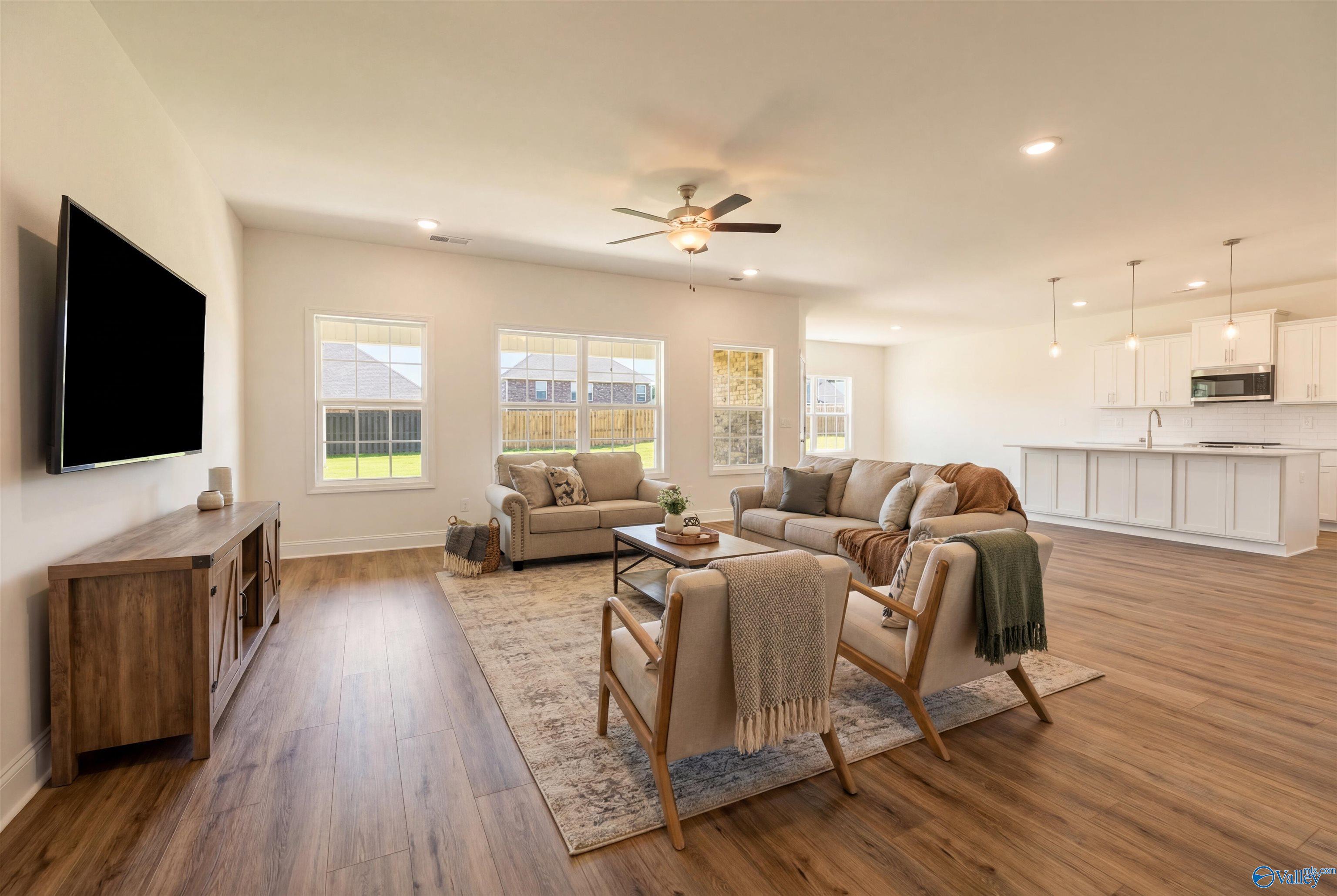Open-concept living room with beige sectional sofa, wooden coffee table, and large windows overlooking backyard in Davidson Homes The Rockford B, Toney, Alabama