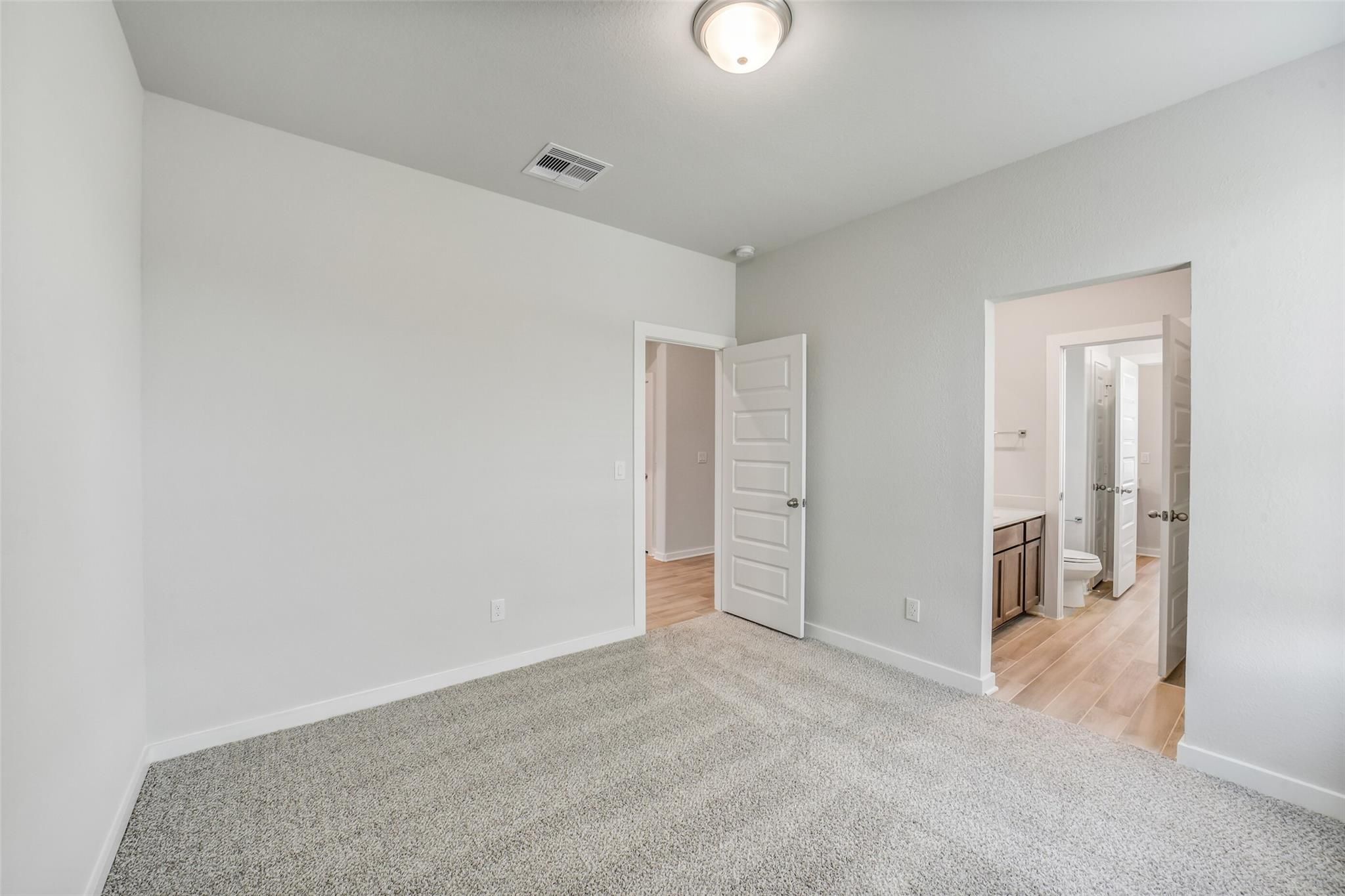 Spacious secondary bedroom with gray carpet, white walls, and attached bath featuring oak vanity and toilet in Davidson Homes Acadia C, Magnolia TX