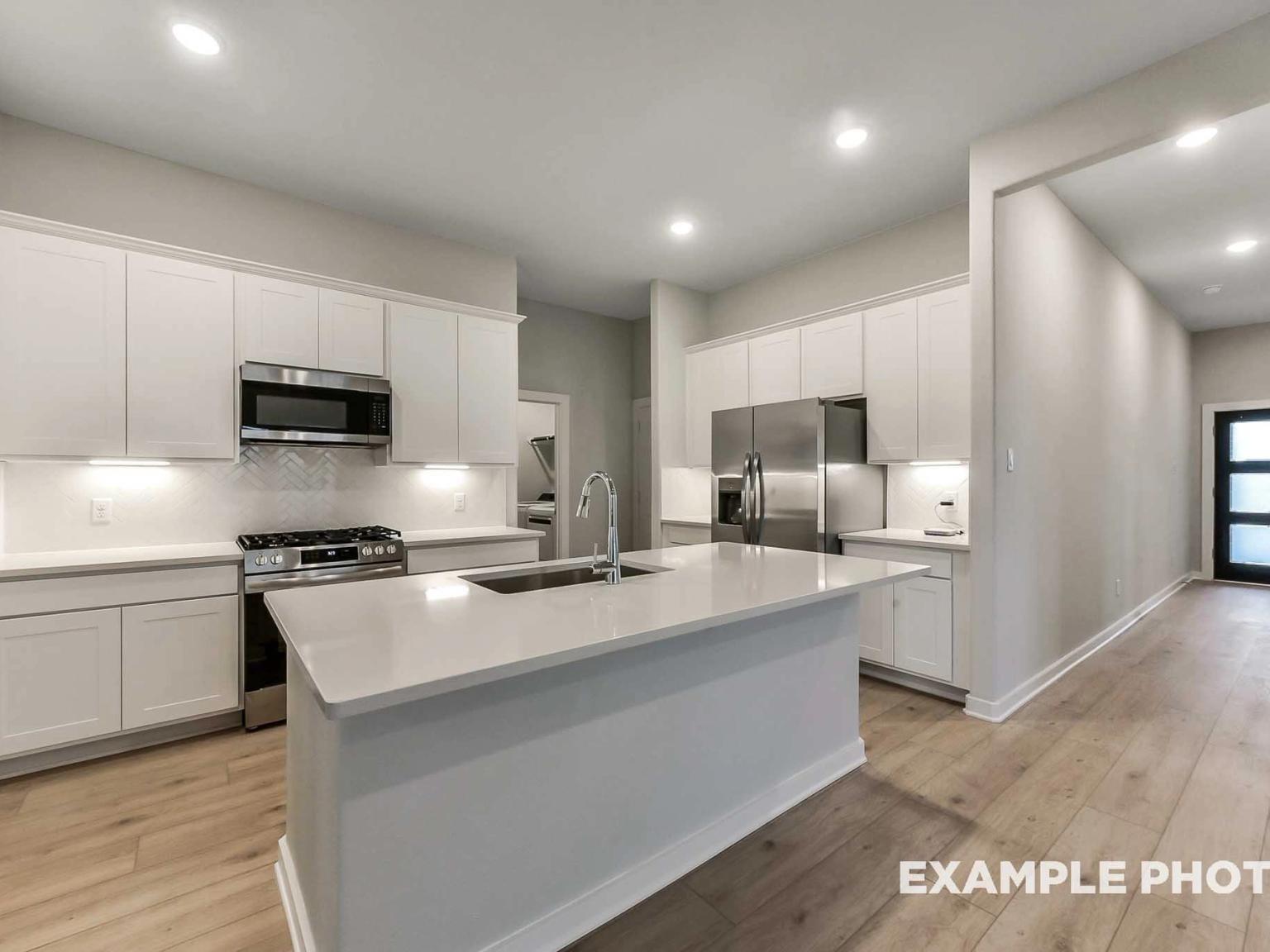 Modern kitchen with white cabinets, quartz island, and stainless steel appliances in Davidson Homes' Brookside F floor plan.