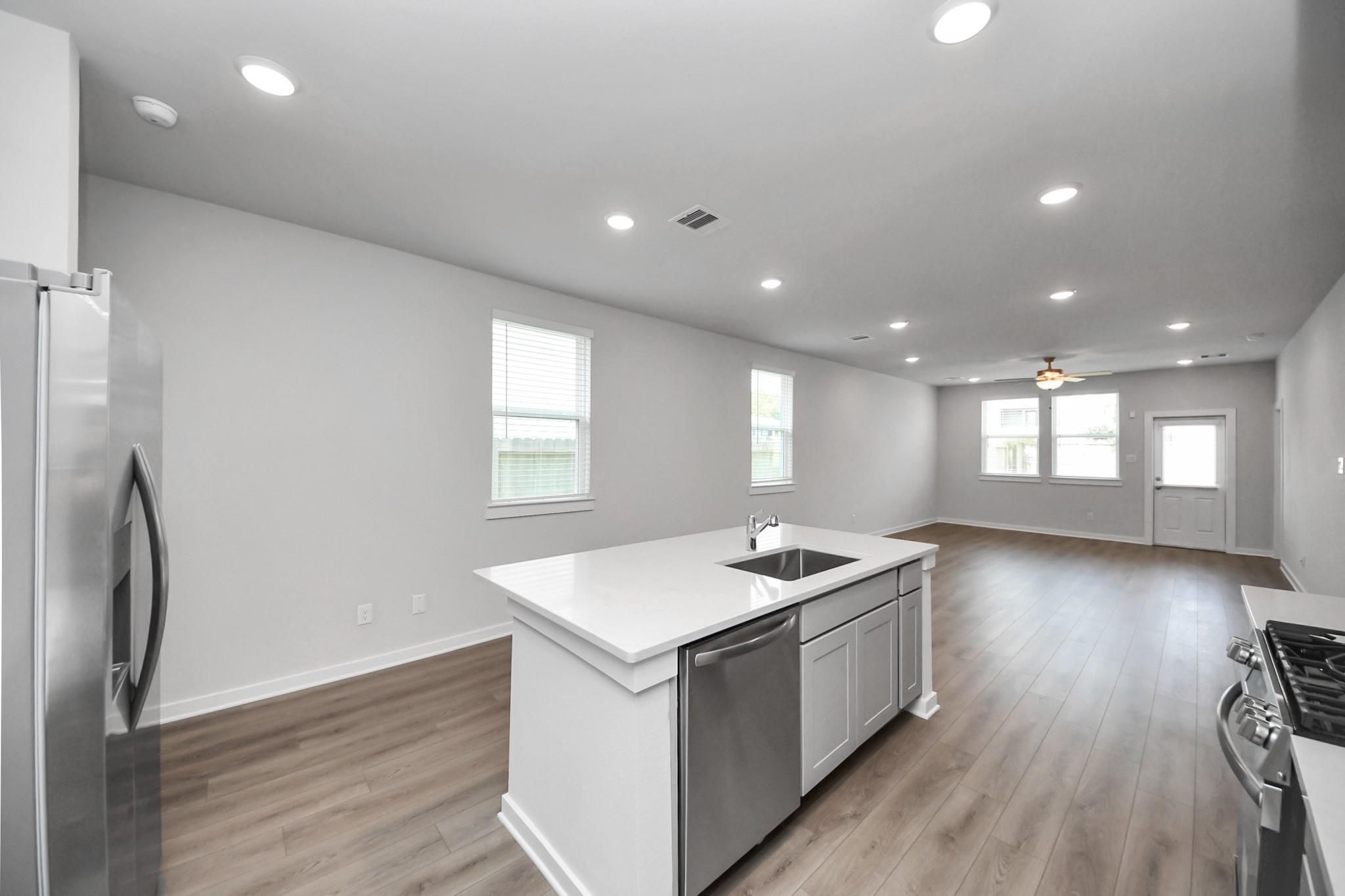 Open-concept kitchen with white island, stainless appliances, and luxury vinyl plank flooring in Davidson Homes The Frio F, Houston