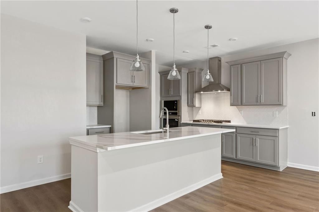 Modern gray cabinet kitchen with white quartz island, stainless steel appliances, pendant lights in Davidson Homes The Marion A, Winder, GA