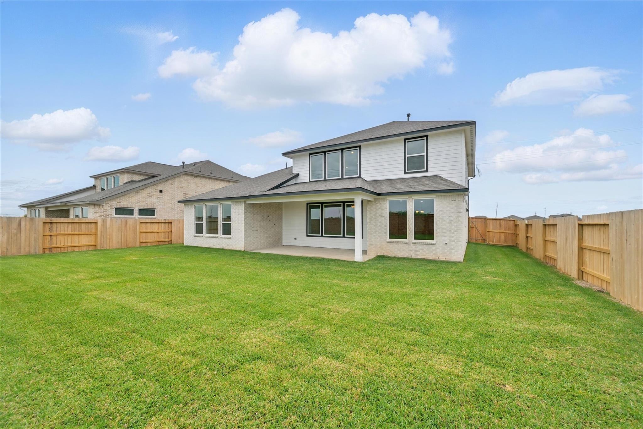 Rear view of The Philip A 4-bedroom home by Davidson Homes with covered patio, large windows, and lush green backyard in Lago Mar, Texas City, Texas