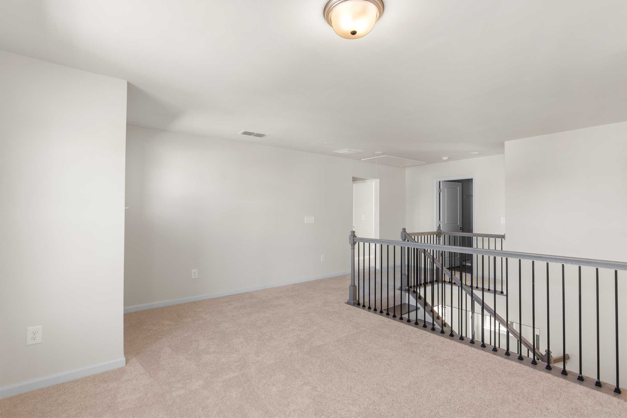 Spacious upper floor hallway in The Willow B home with beige carpet, white walls, black metal railing, and bedroom doorways