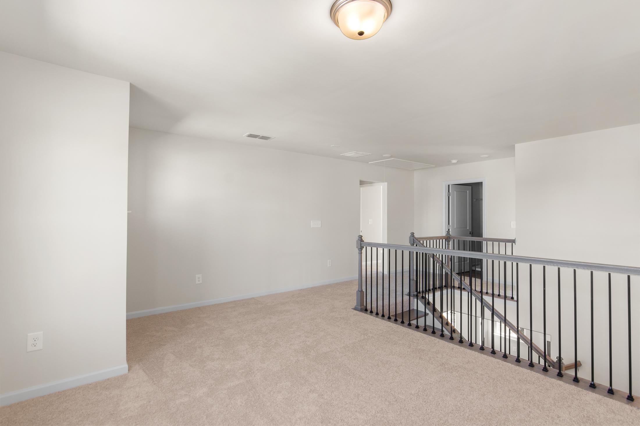 Spacious upper floor hallway in The Willow B home with beige carpet, white walls, black metal railing, and bedroom doorways