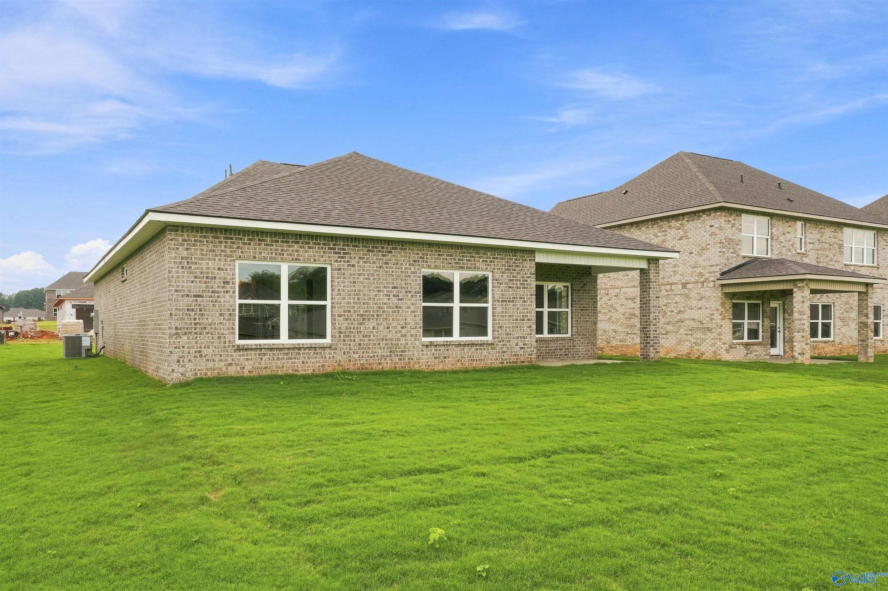 Rear exterior of brick 1-story Davidson Homes Franklin C with covered patio and large backyard in The Meadows, Athens, Alabama