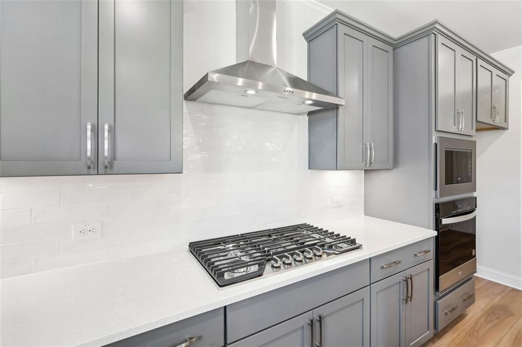 Modern kitchen with gray cabinets, stainless steel range hood, and gas cooktop in The Hickory C home, Hoschton, Georgia.