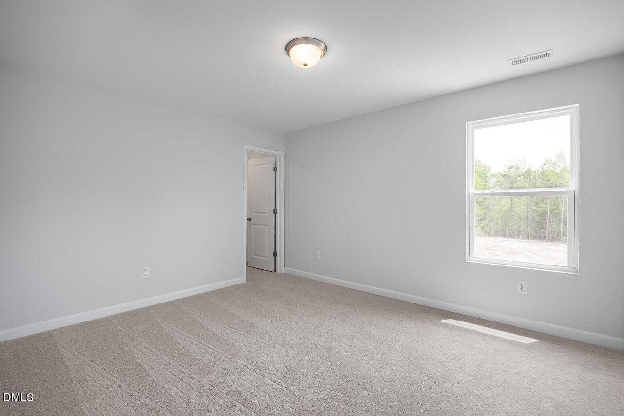 Spacious empty bedroom with light gray walls, large window overlooking trees, carpeted floor in Davidson Homes The Hickory II B, Zebulon NC