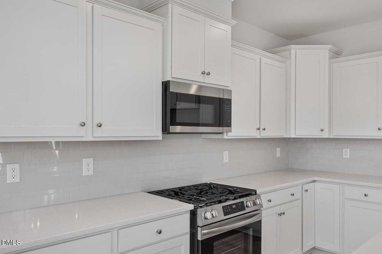 Modern white shaker kitchen with stainless steel microwave, oven, gas cooktop, and gray subway tile backsplash in The Graham Exterior, Fuquay-Varina, NC