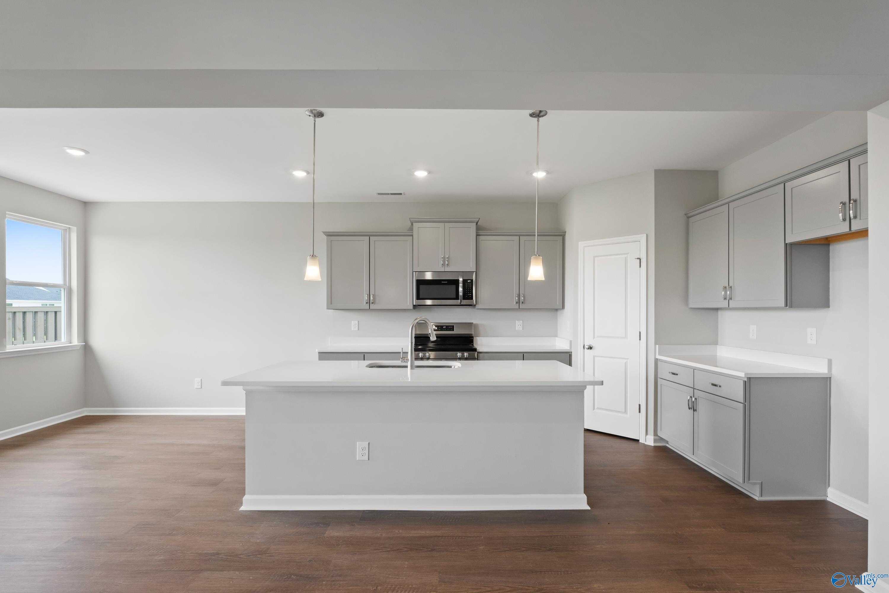 Modern white kitchen with central island, stainless microwave, pendant lights in Davidson Homes The Dorado, Athens AL