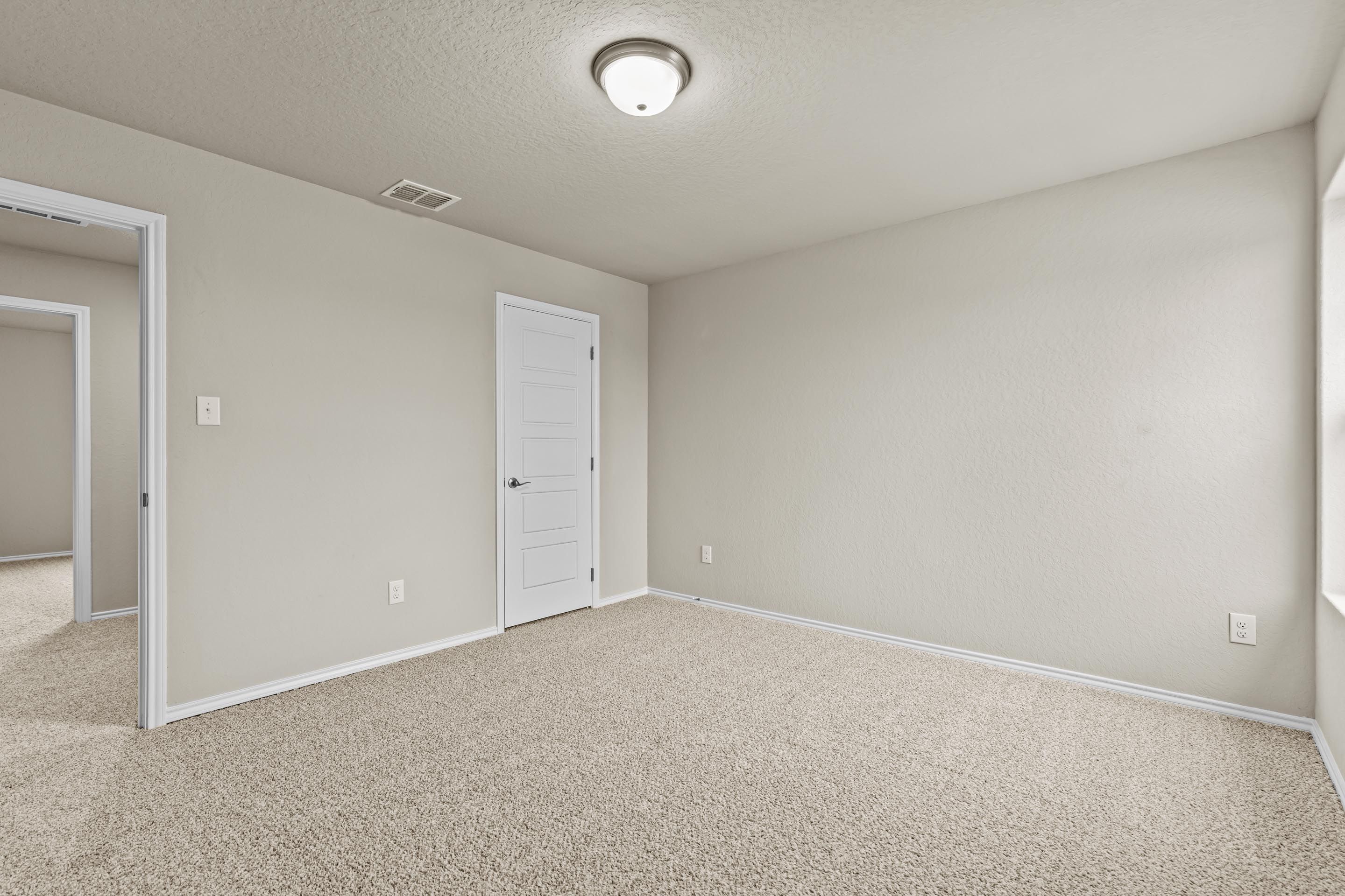 Bright secondary bedroom with neutral beige walls, carpet flooring, closet door, and window in Davidson Homes The Douglas F, San Antonio