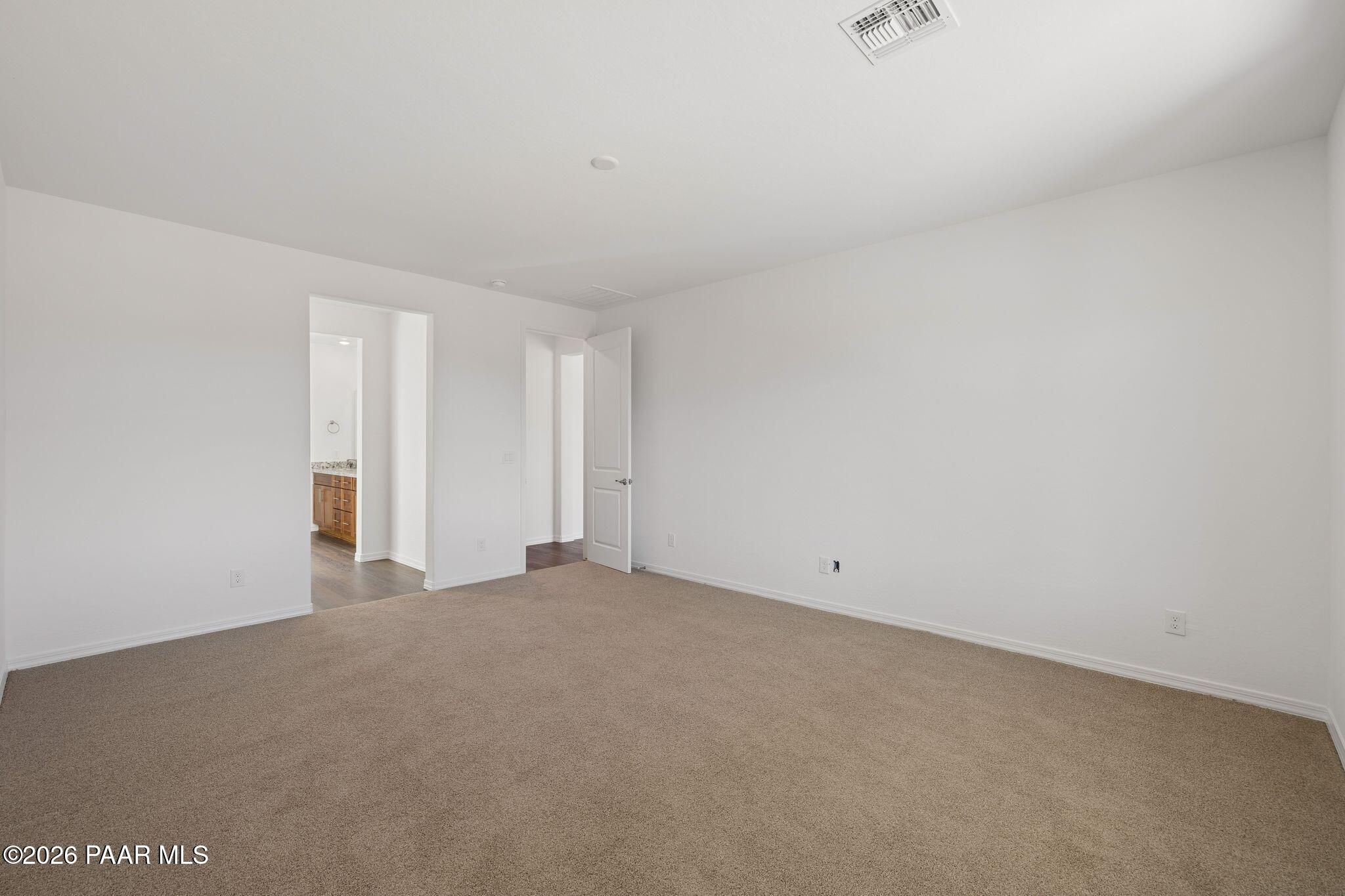 Spacious empty bedroom featuring beige carpet, white walls, and adjacent bathroom with oak cabinets in Davidson Homes The Monarch A, Prescott AZ