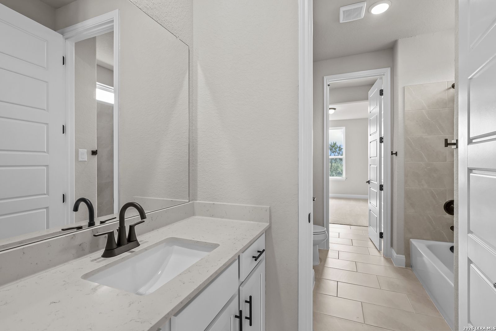 Bathroom with white vanity, quartz countertop, matte black faucet, and tile tub shower in Davidson Homes Foster E plan, Castroville, TX