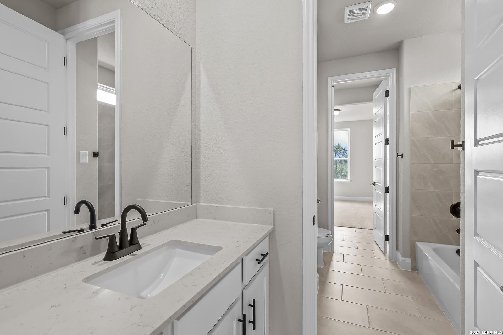 Bathroom with white vanity, quartz countertop, matte black faucet, and tile tub shower in Davidson Homes Foster E plan, Castroville, TX