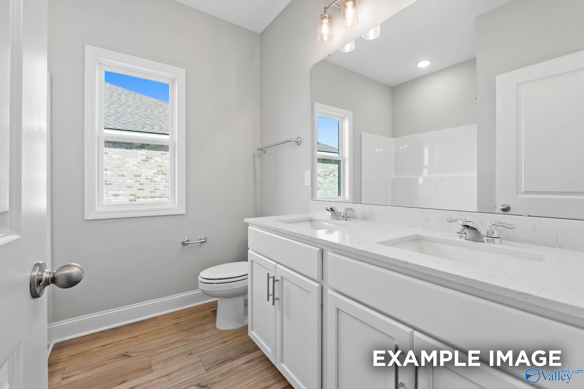 Modern bathroom with double vanity, quartz countertops, and wood-style flooring in The Everett C home at Anderson Farm.
