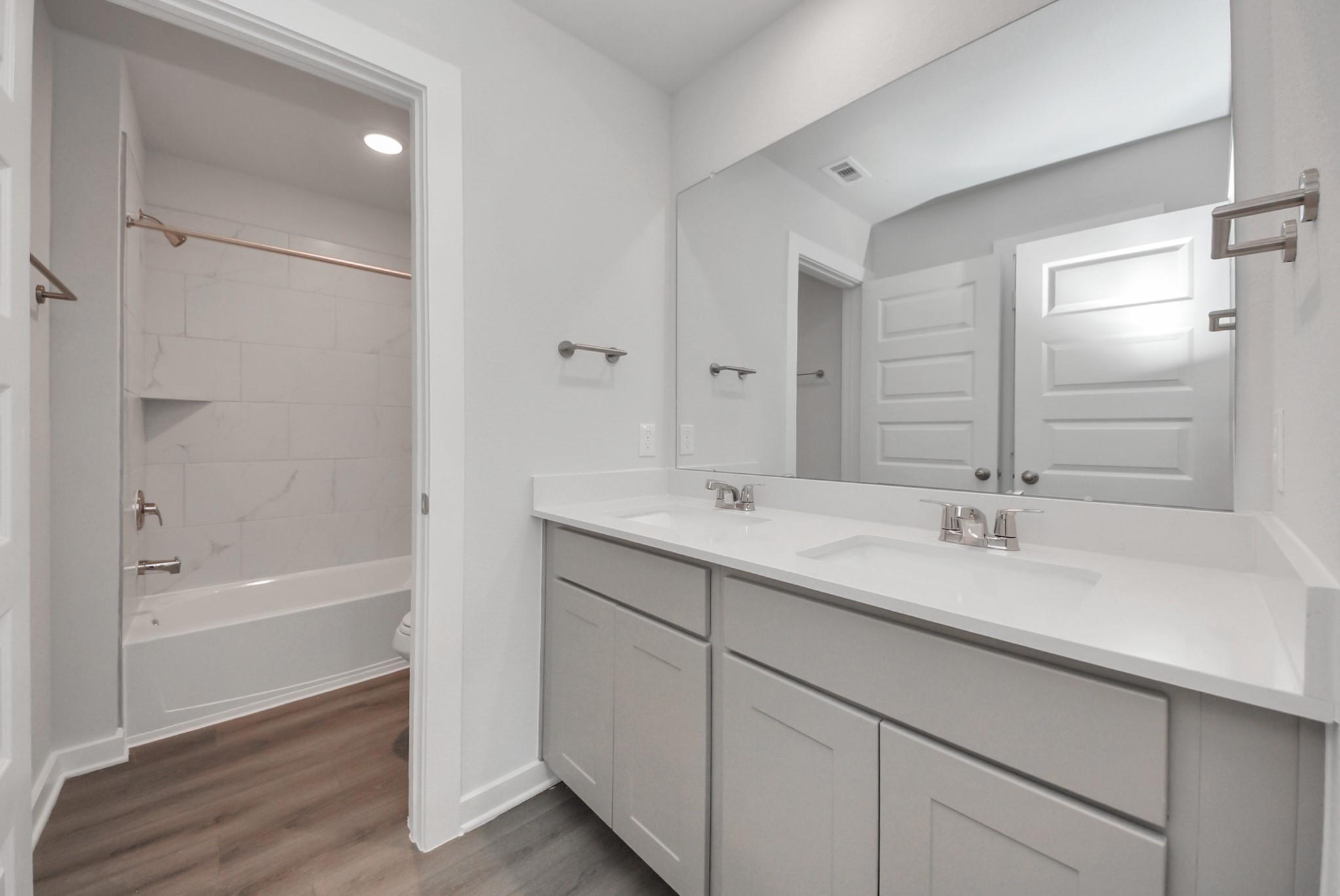 Double vanity bathroom with white quartz counters and tile tub shower in Davidson Homes San Marcos E, Beasley, Texas