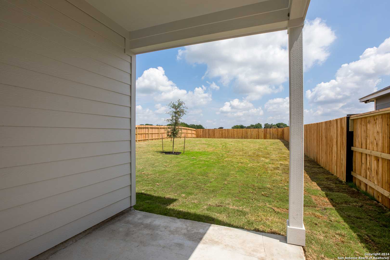Covered back patio overlooking fenced backyard with green lawn and young tree in Davidson Homes The Murray H, Seguin, Texas
