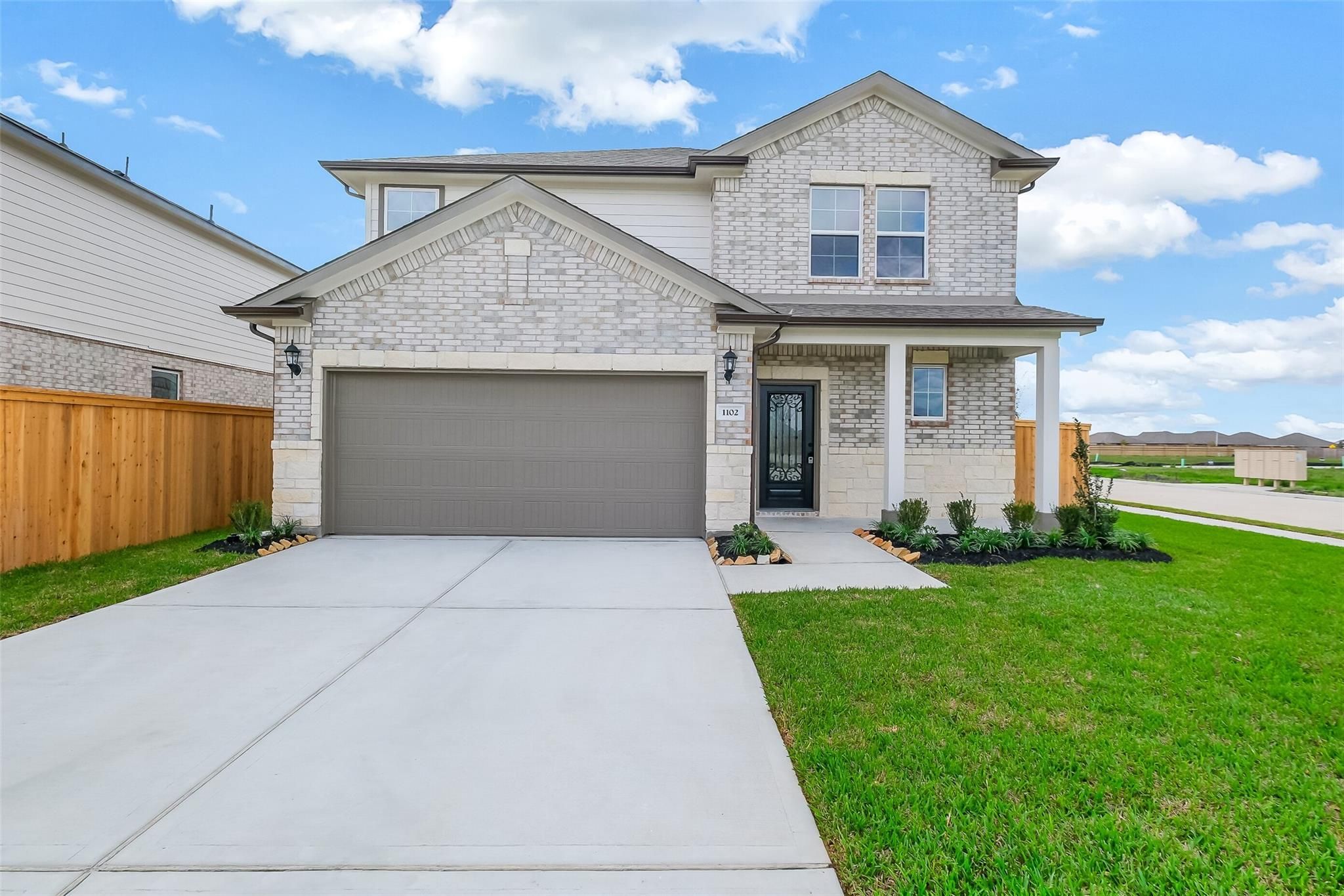 Modern two-story brick home with two-car garage, front porch, and landscaped yard in Emberly, Beasley, Texas - Davidson Homes Tierra B