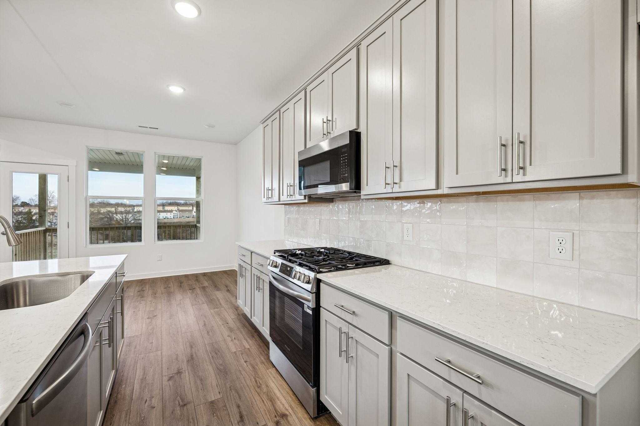 Bright kitchen with white shaker cabinets, quartz counters, stainless gas range overlooking deck in Davidson Homes The Willow, Calista Farms TN