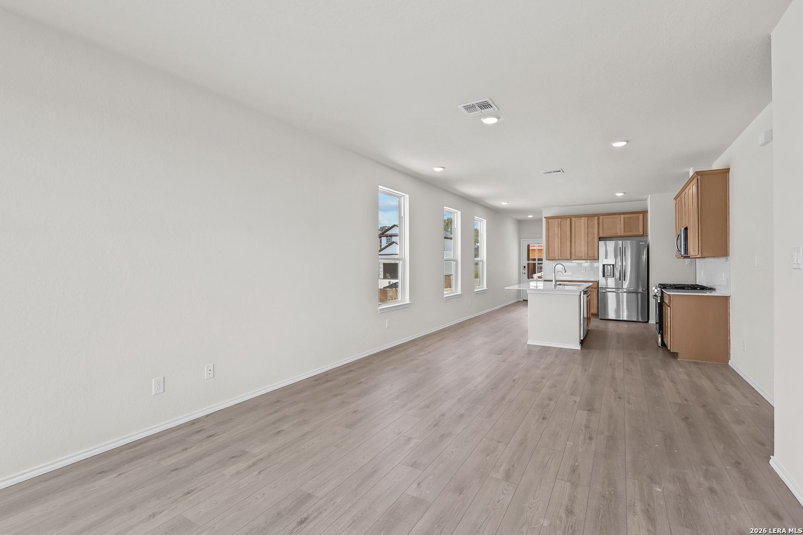 Open-concept kitchen and living area with wood-style flooring in The Gillian B floor plan, Meadows at Oak Creek, San Antonio.