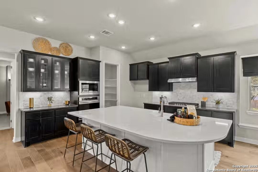 Modern kitchen featuring black cabinets, white quartz island, rattan bar stools in Davidson Homes The Summerlin B, Castroville, Texas