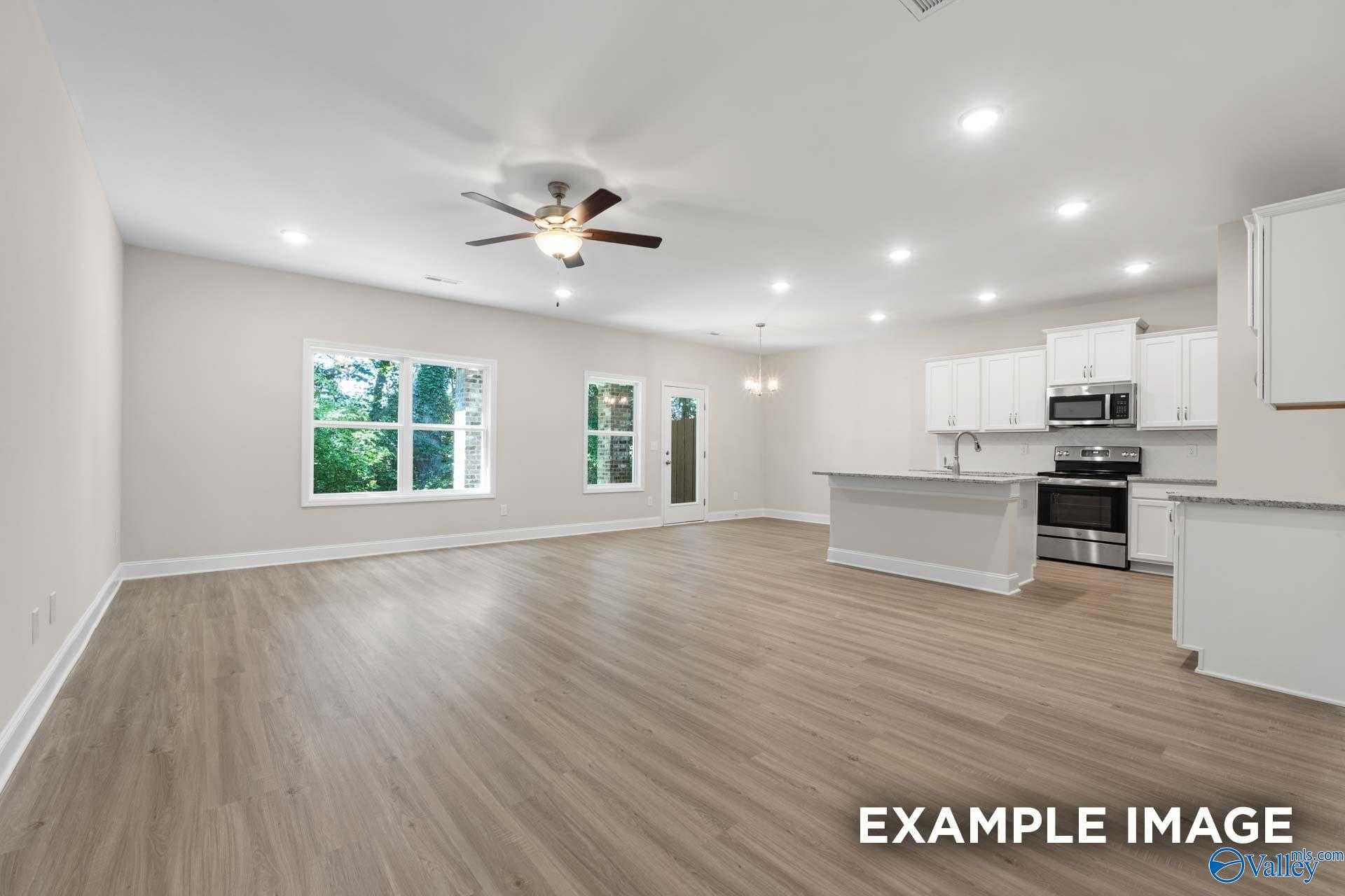 Spacious open-concept living room with hardwood floors, ceiling fan, large windows, and modern kitchen island in The Camden C, Huntsville, AL