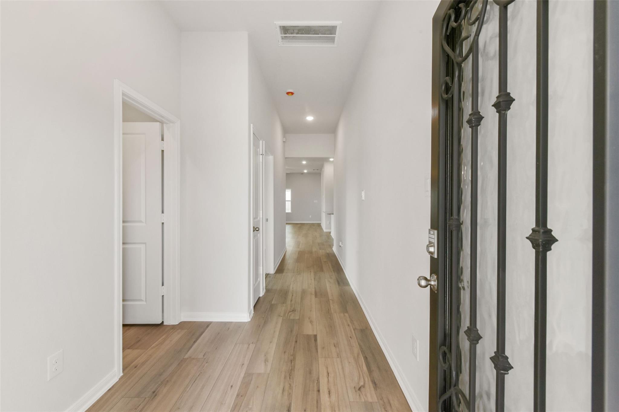 Bright hallway with light wood floors, white walls, and decorative entry door in Davidson Homes The Laguna B, Magnolia, Texas