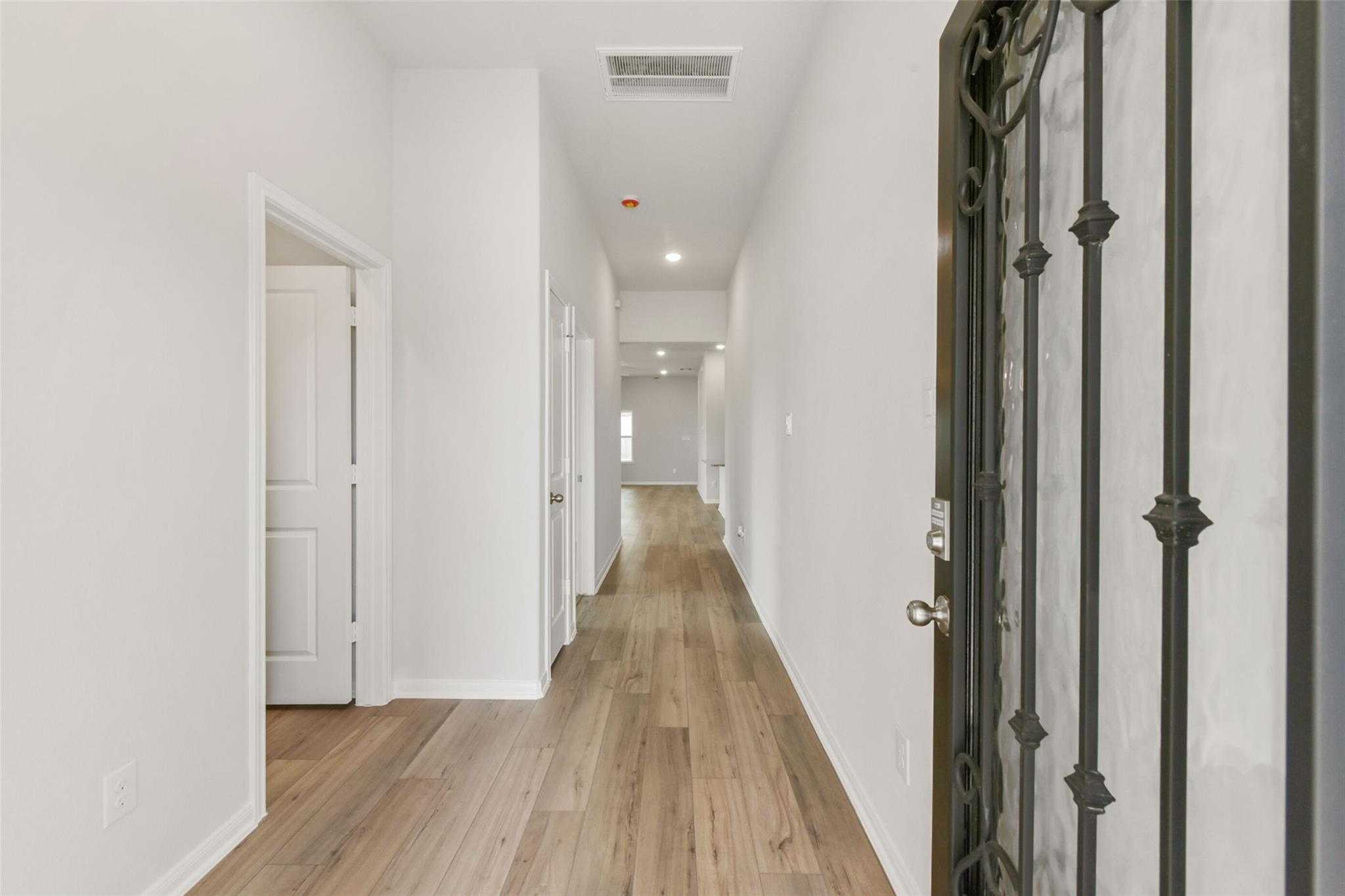 Elegant hallway with light wood floors, white walls, and arched doorways in Davidson Homes The Laguna B, Magnolia, Texas
