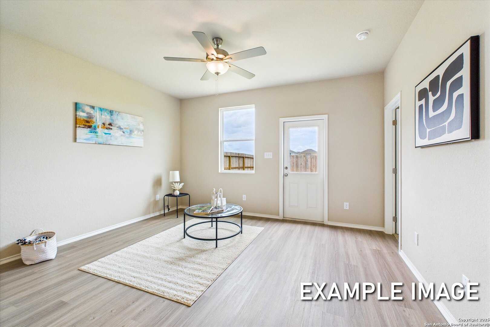 Bright living room with ceiling fan, abstract wall art, sliding glass door, and hardwood floors in Davidson Homes The Comal B, Agave, San Antonio