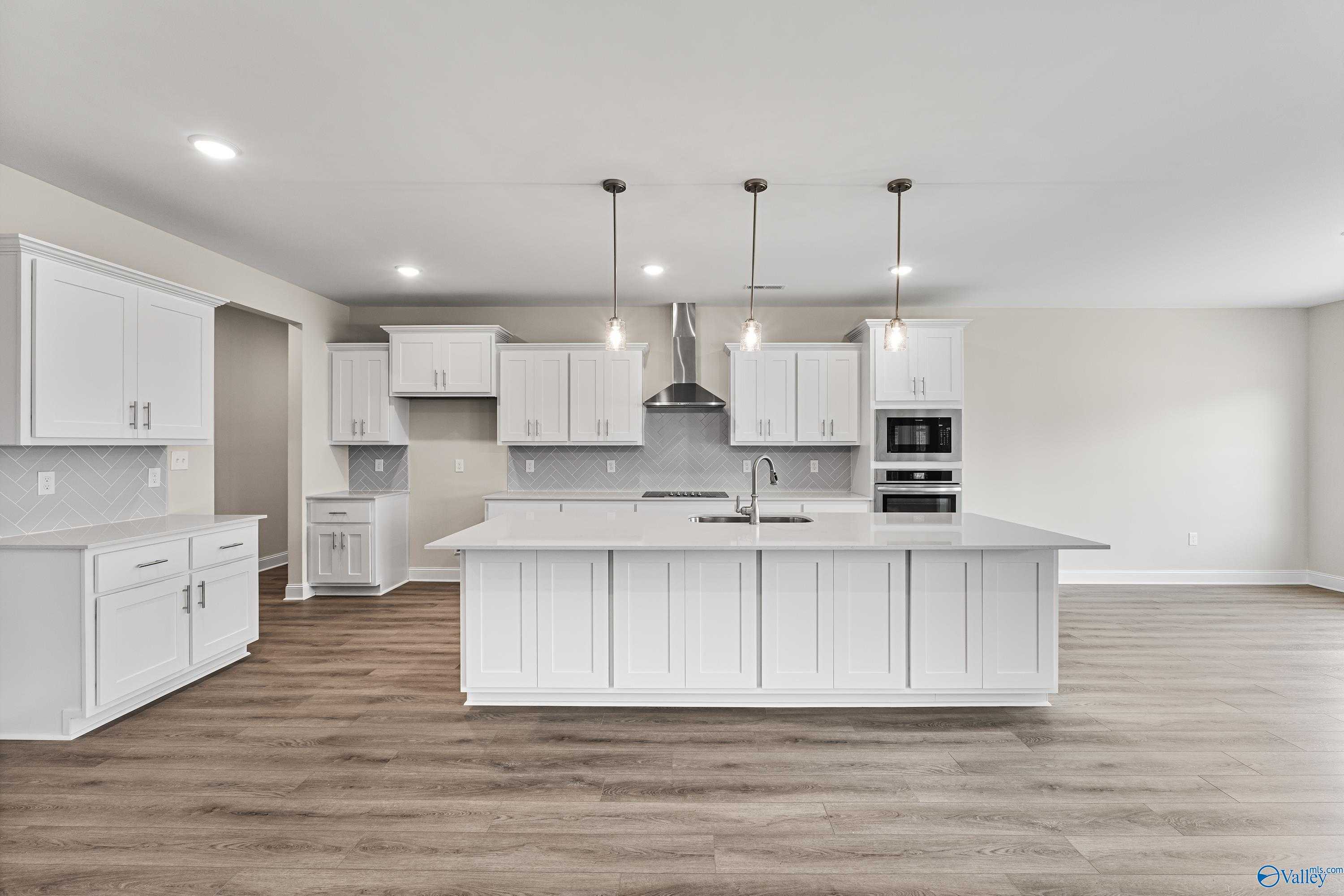 Modern white kitchen featuring large center island, stainless steel appliances, subway tile backsplash, and hardwood floors in The Finleigh by Davidson Homes, Toney, Alabama