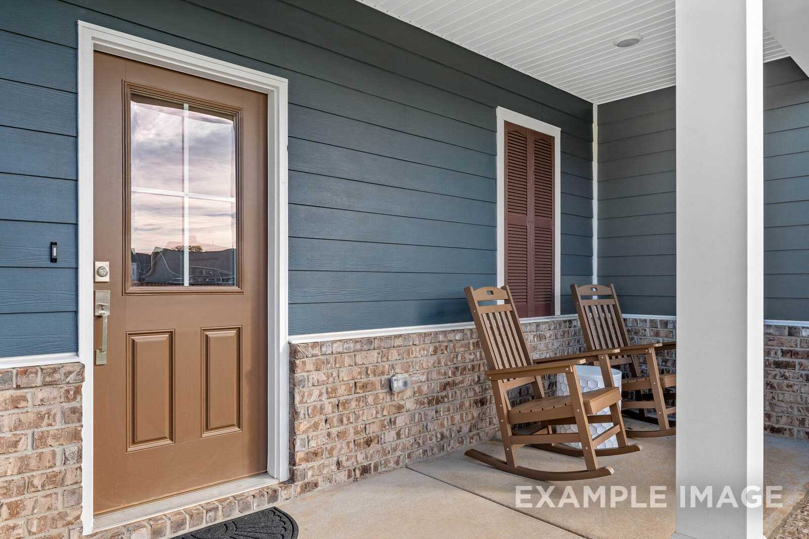 Cozy front porch of The Gordon B home with blue siding, brick accents, wooden door, and rocking chairs