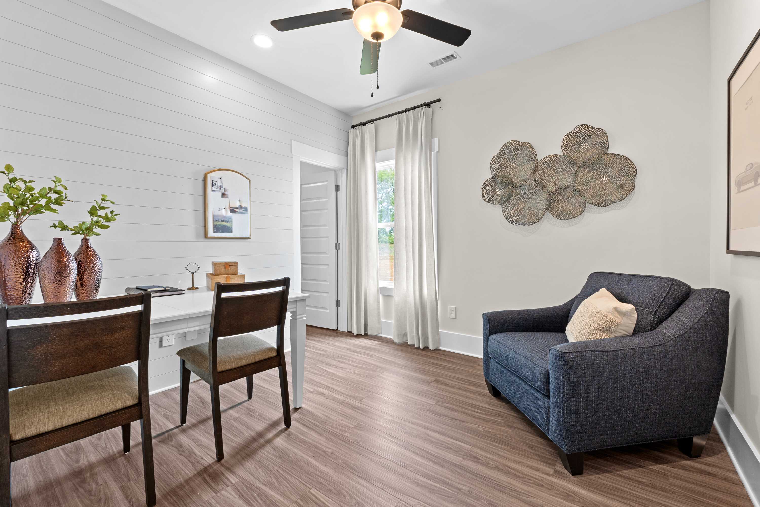 Cozy home office at Ivy Hills in Toney Alabama with shiplap walls, wooden desk, navy armchair, and hardwood floors