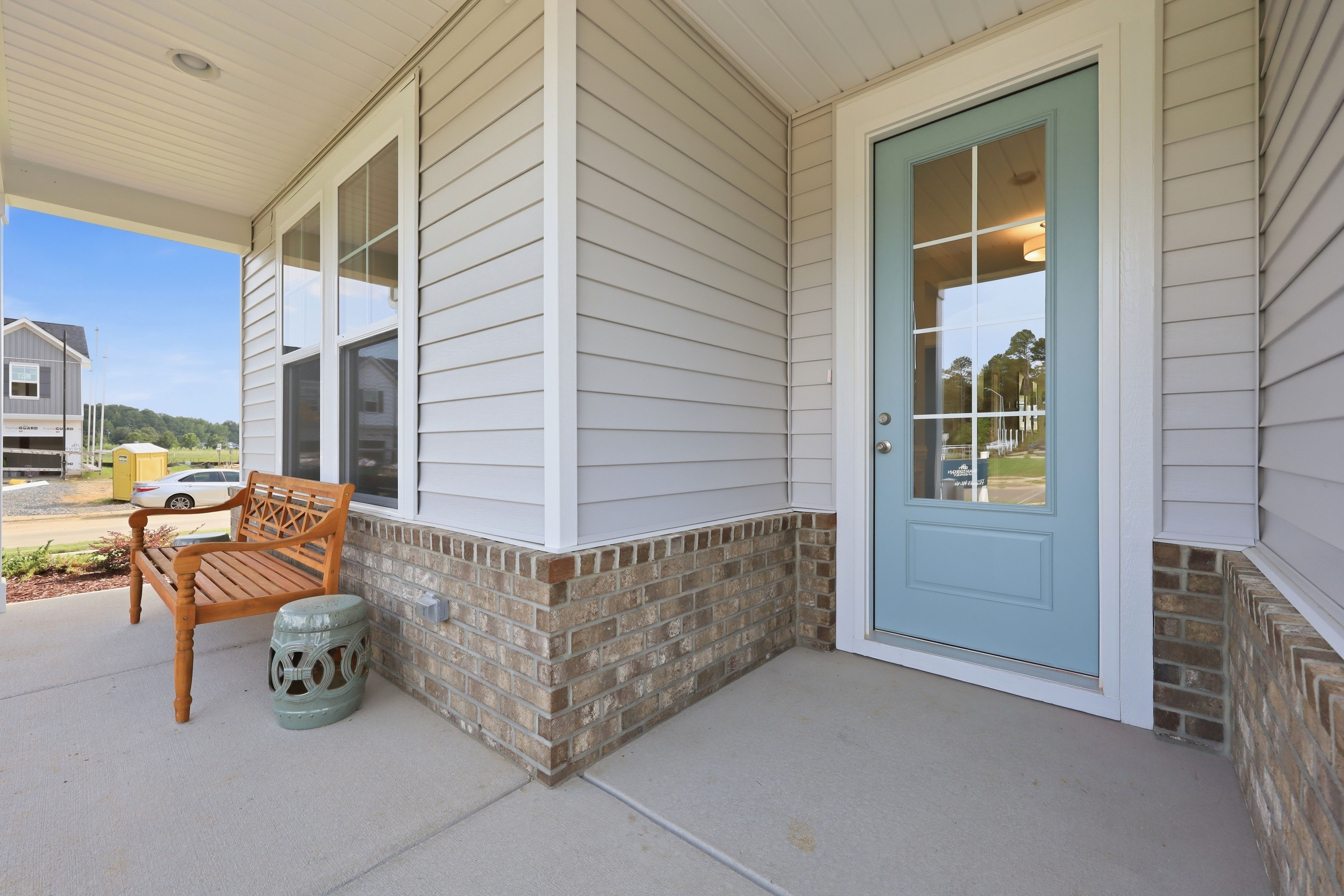 Welcoming front porch of The Daphne home design featuring a light blue door, brick accents, and charming wooden bench.
