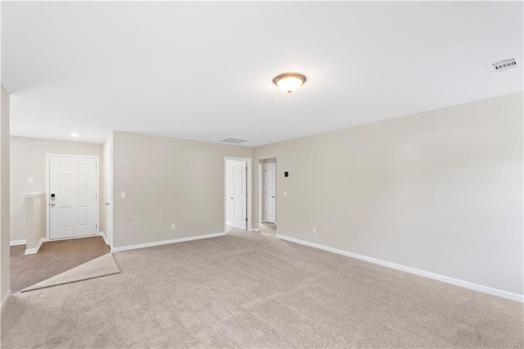 Spacious empty living room with beige walls, tan carpet, and multiple doors in Davidson Homes The Washington, Phenix City, Alabama