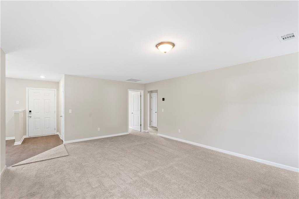 Spacious empty living room with beige walls, tan carpet, and multiple doors in Davidson Homes The Washington, Phenix City, Alabama