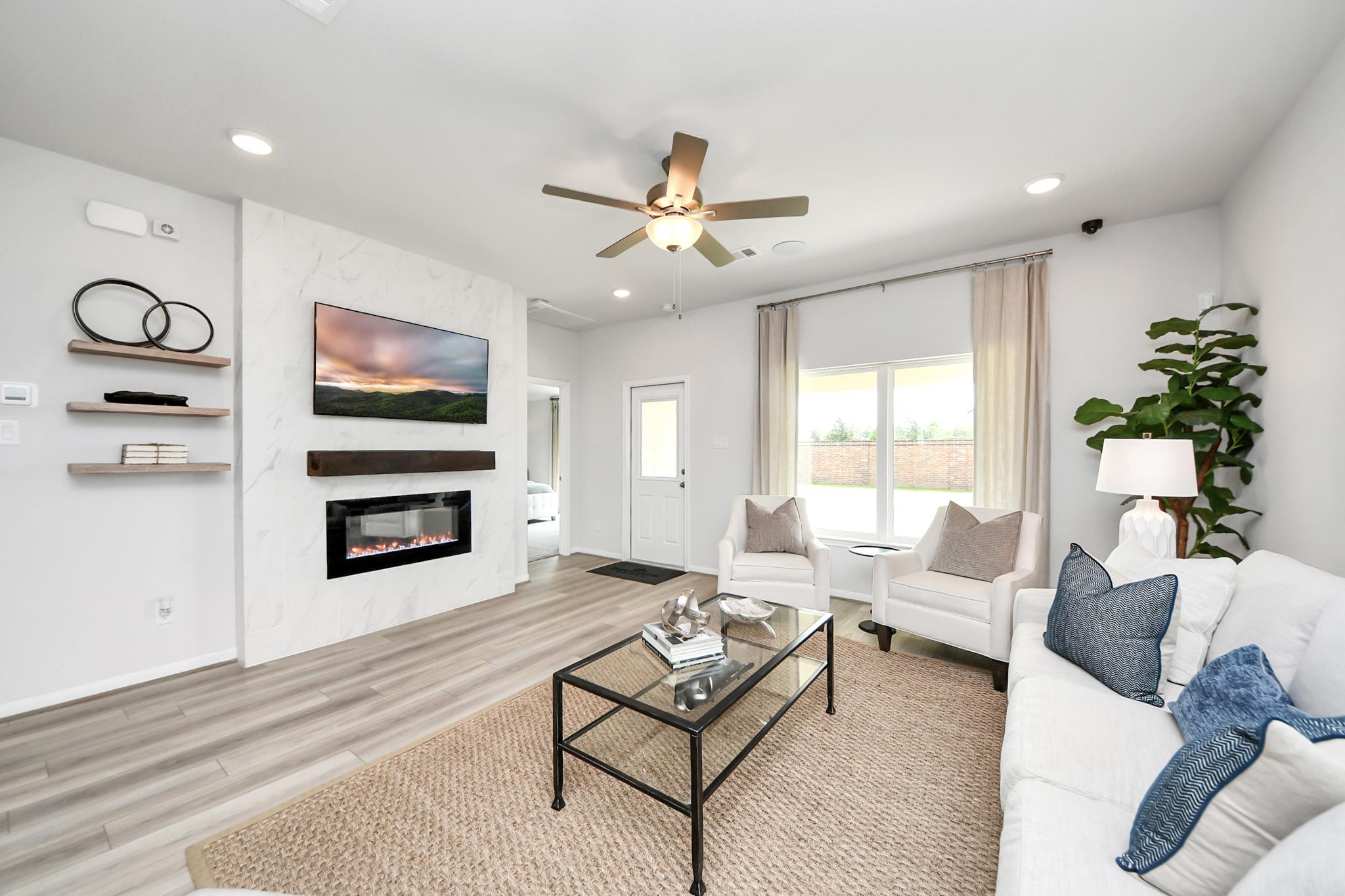 Modern living room in Sunterra by Davidson Homes, Katy, TX, featuring a marble fireplace, wall-mounted TV, and chic decor.