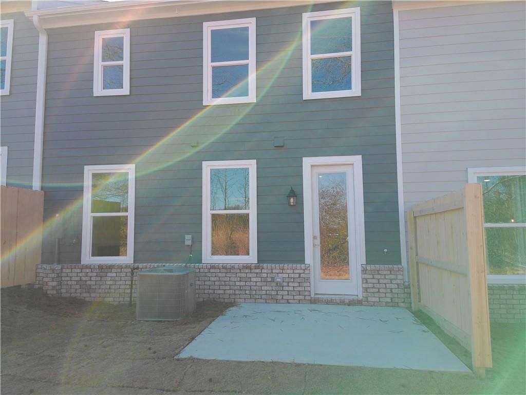 Back view of two-story Marion C home with gray siding, white-framed windows, back door, concrete patio, and wood fence in Lake Shore, Winder, Georgia
