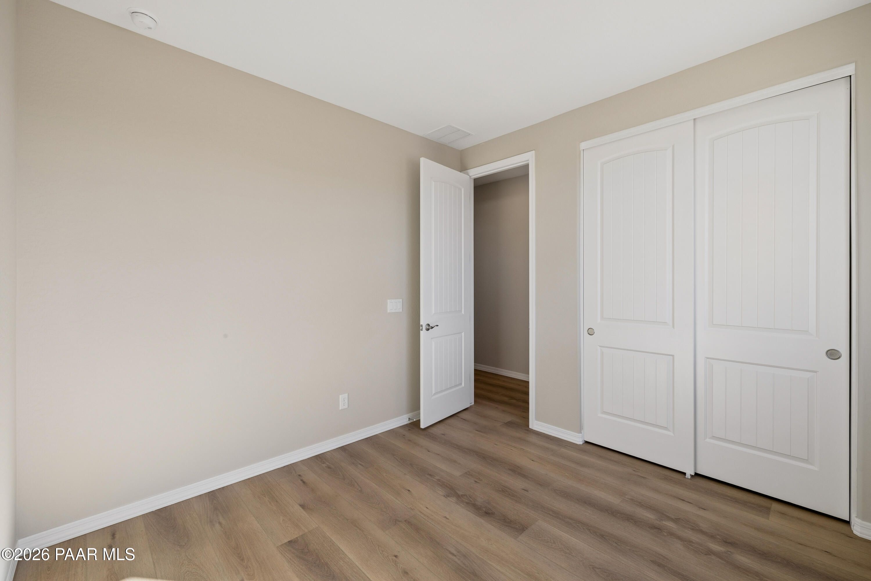Empty bedroom featuring beige walls, bifold closet doors, open interior doorway, and luxury vinyl plank flooring in Davidson Homes The Harmony A, Prescott Valley