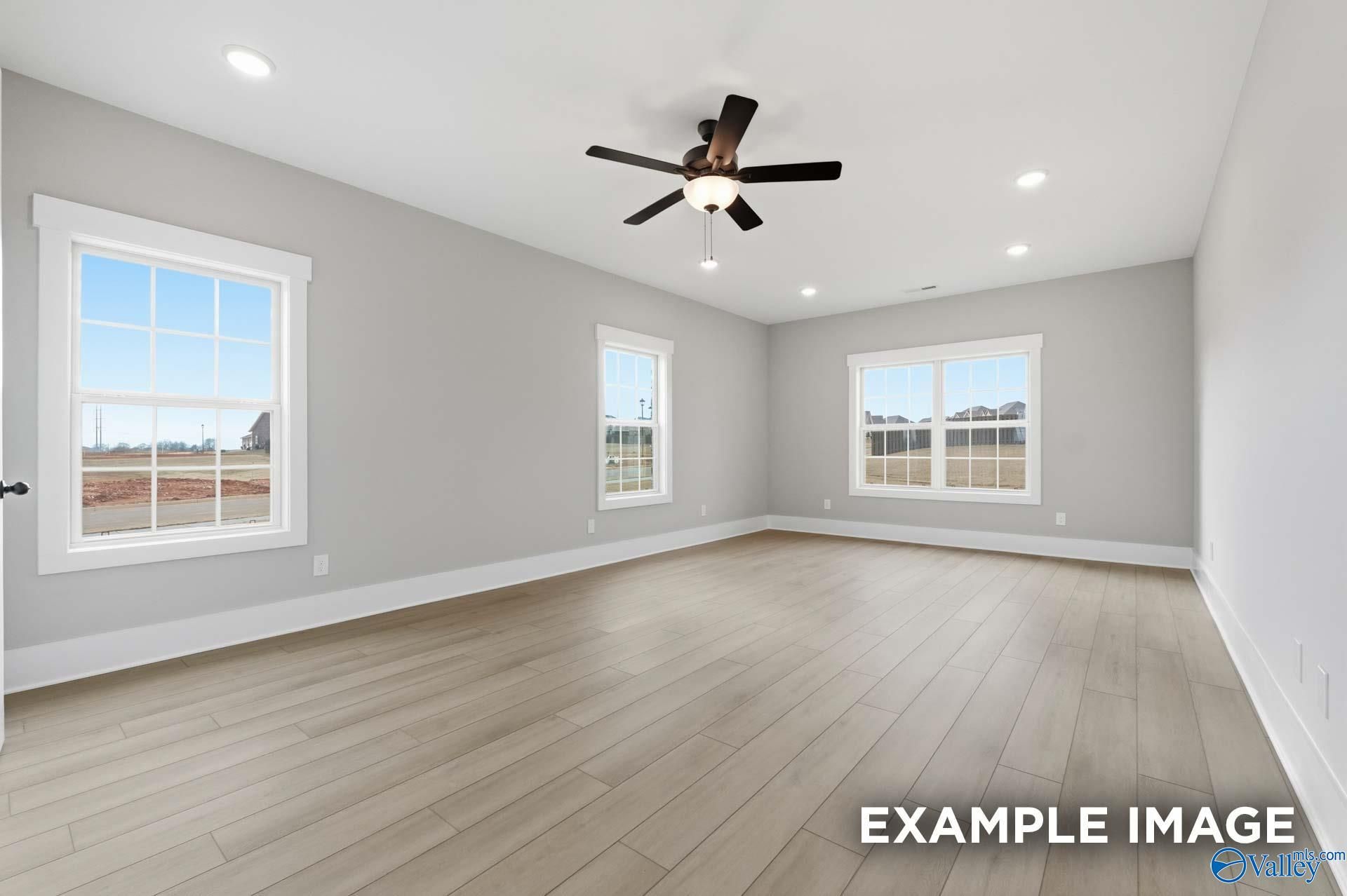 Bright empty bedroom with light gray walls, hardwood floors, large sunny windows, and ceiling fan in Davidson Homes The Emory, Decatur AL
